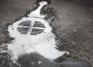 White paint flows into the manhole. Pollution metaphor