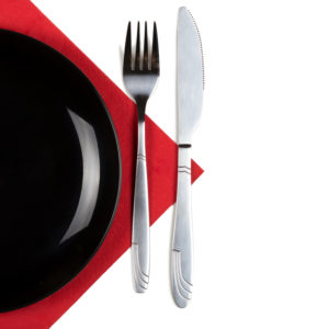 Black plate, fork and knife on red napkin. Isolated on white. Square format.